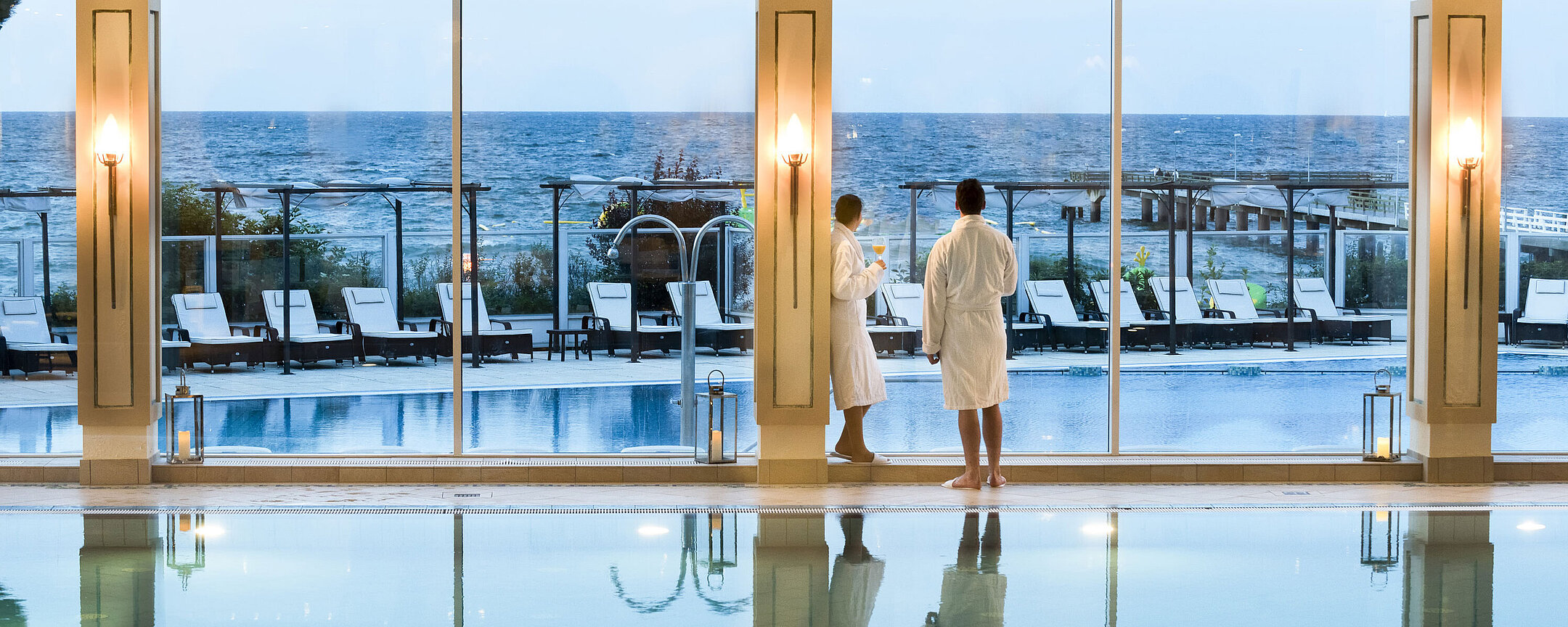 Schwimmbad Innenpool mit Meerblick im Maritim Seehotel Timmendorfer Strand, zwei Gäste in Bademänteln am Fenster.