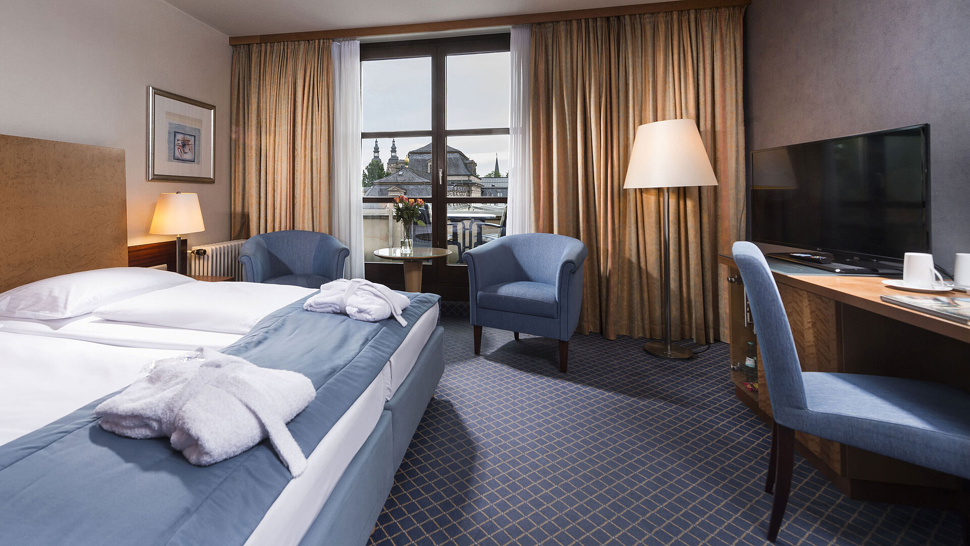 Elegantes Superior Zimmer im Maritim Hotel Fulda mit Doppelbett, Sitzbereich und Balkon mit Blick auf die Stadt.