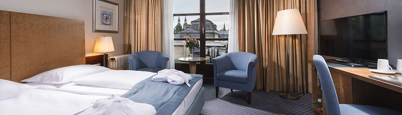 Superior Zimmer Elegantes Superior Zimmer im Maritim Hotel Fulda mit Doppelbett, Sitzbereich und Balkon mit Blick auf die Stadt.