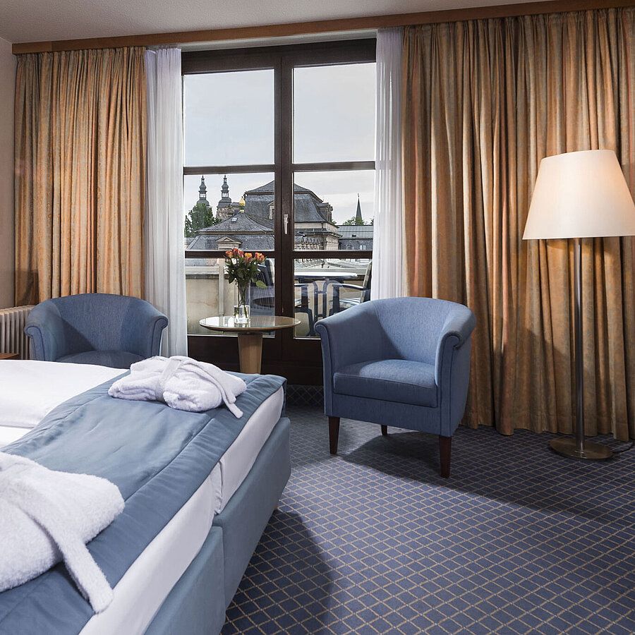 Elegantes Superior Zimmer im Maritim Hotel Fulda mit Doppelbett, Sitzbereich und Balkon mit Blick auf die Stadt.