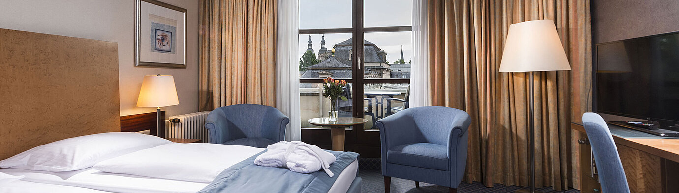 Superior Zimmer Elegantes Superior Zimmer im Maritim Hotel Fulda mit Doppelbett, Sitzbereich und Balkon mit Blick auf die Stadt.