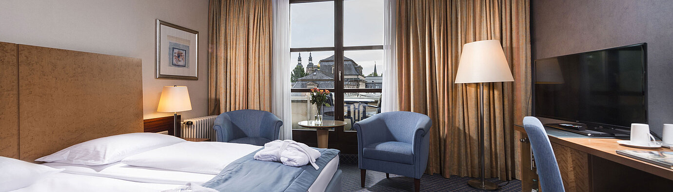 Elegantes Superior Zimmer im Maritim Hotel Fulda mit Doppelbett, Sitzbereich und Balkon mit Blick auf die Stadt.