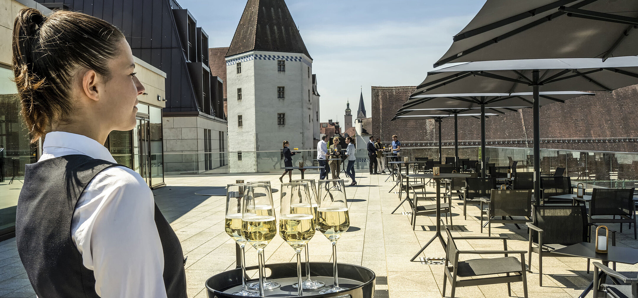 Kellnerin serviert Getränke auf der sonnigen Dachterrasse im Maritim Hotel Ingolstadt.