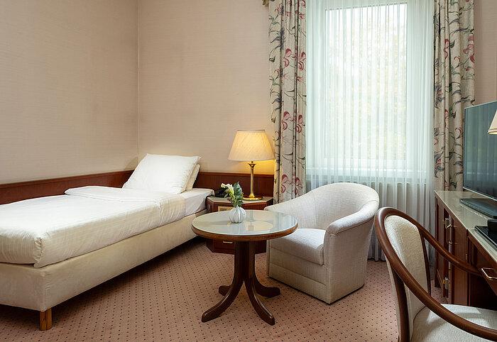 Classic Einzelzimmer mit Bett, Sitzecke, Schreibtisch und großem Fenster im hellen, klassischen Design im Maritim Hotel Bad Wildungen.