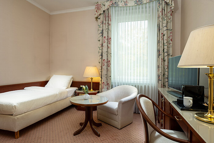 Classic Einzelzimmer mit Bett, Sitzecke, Schreibtisch und großem Fenster im hellen, klassischen Design im Maritim Hotel Bad Wildungen.