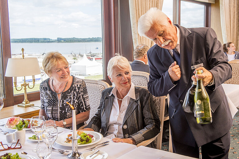 Ein Kellner präsentiert Gästen im Restaurant des Maritim Hotel Travemünde eine exklusive Weinauswahl.