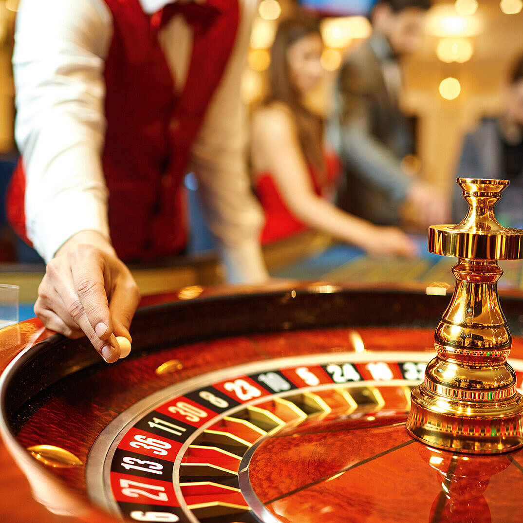 Croupier dreht das Roulette im Casino, während Gäste gespannt auf den Spielverlauf warten.
