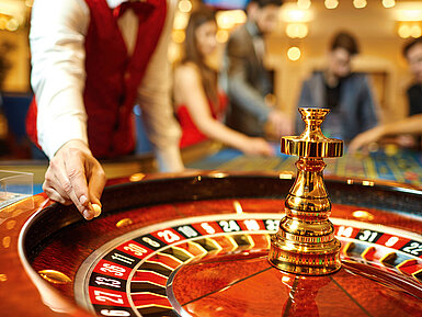 Croupier dreht das Roulette im Casino, während Gäste gespannt auf den Spielverlauf warten.
