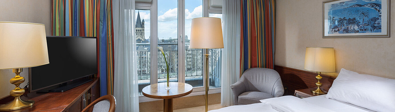 Classic Zimmer im Maritim Hotel Köln mit Doppelbett, Schreibtisch und Blick auf den Rhein sowie das historische Stadtzentrum.