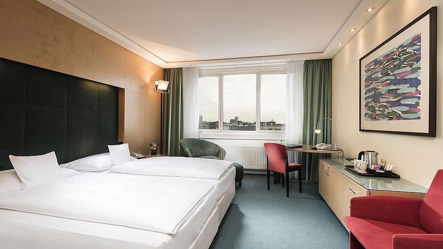 Comfort Zimmer im Maritim proArte Hotel Berlin mit Doppelbett, Schreibtisch, Sessel und Ausblick auf die Stadt.