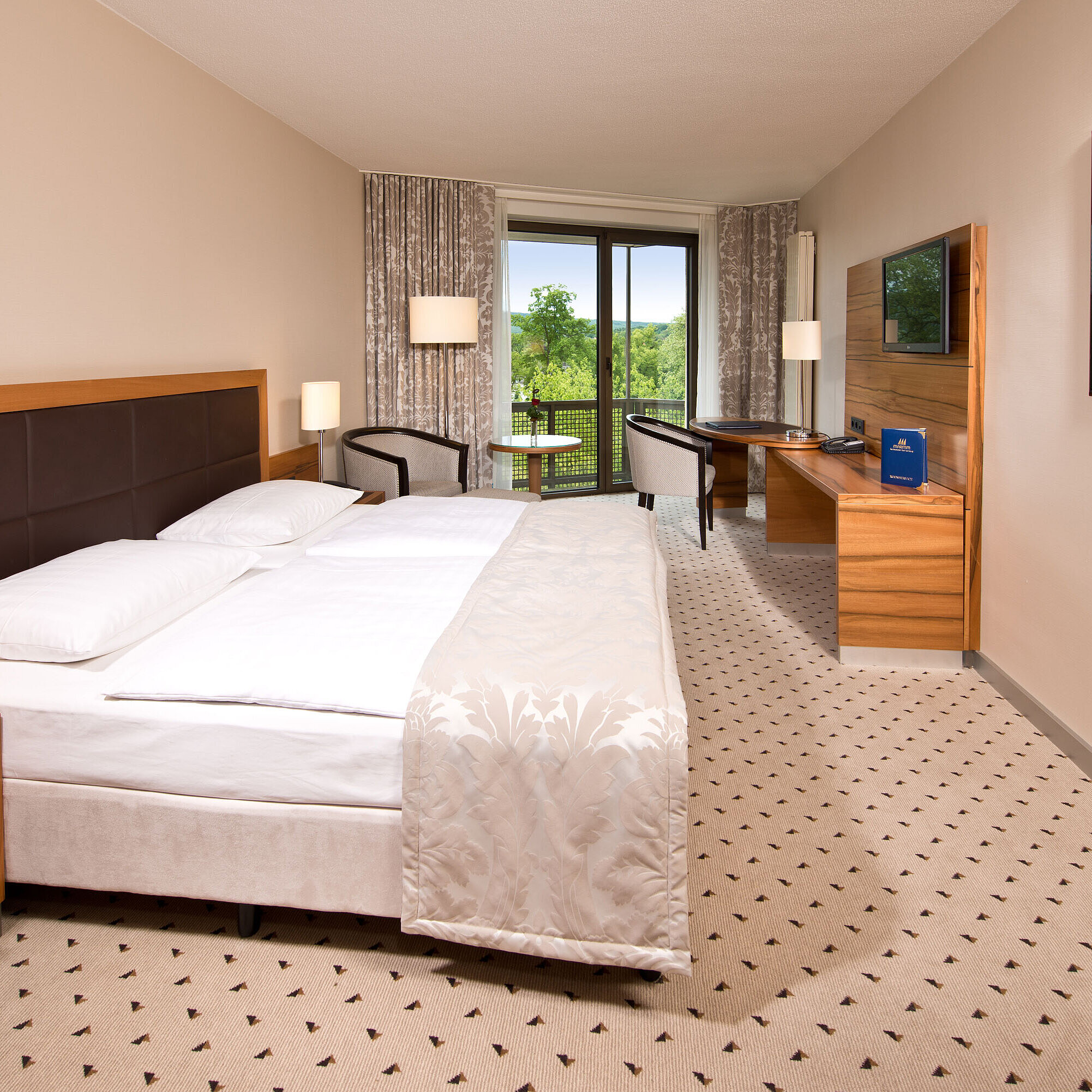 Helles Zimmer im Maritim Hotel Bad Homburg mit gemütlichem Bett, Schreibtisch und Balkon mit grünem Ausblick.