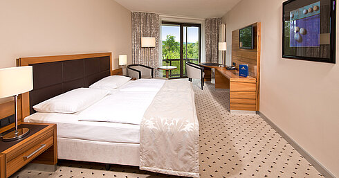 Helles Zimmer im Maritim Hotel Bad Homburg mit gemütlichem Bett, Schreibtisch und Balkon mit grünem Ausblick.