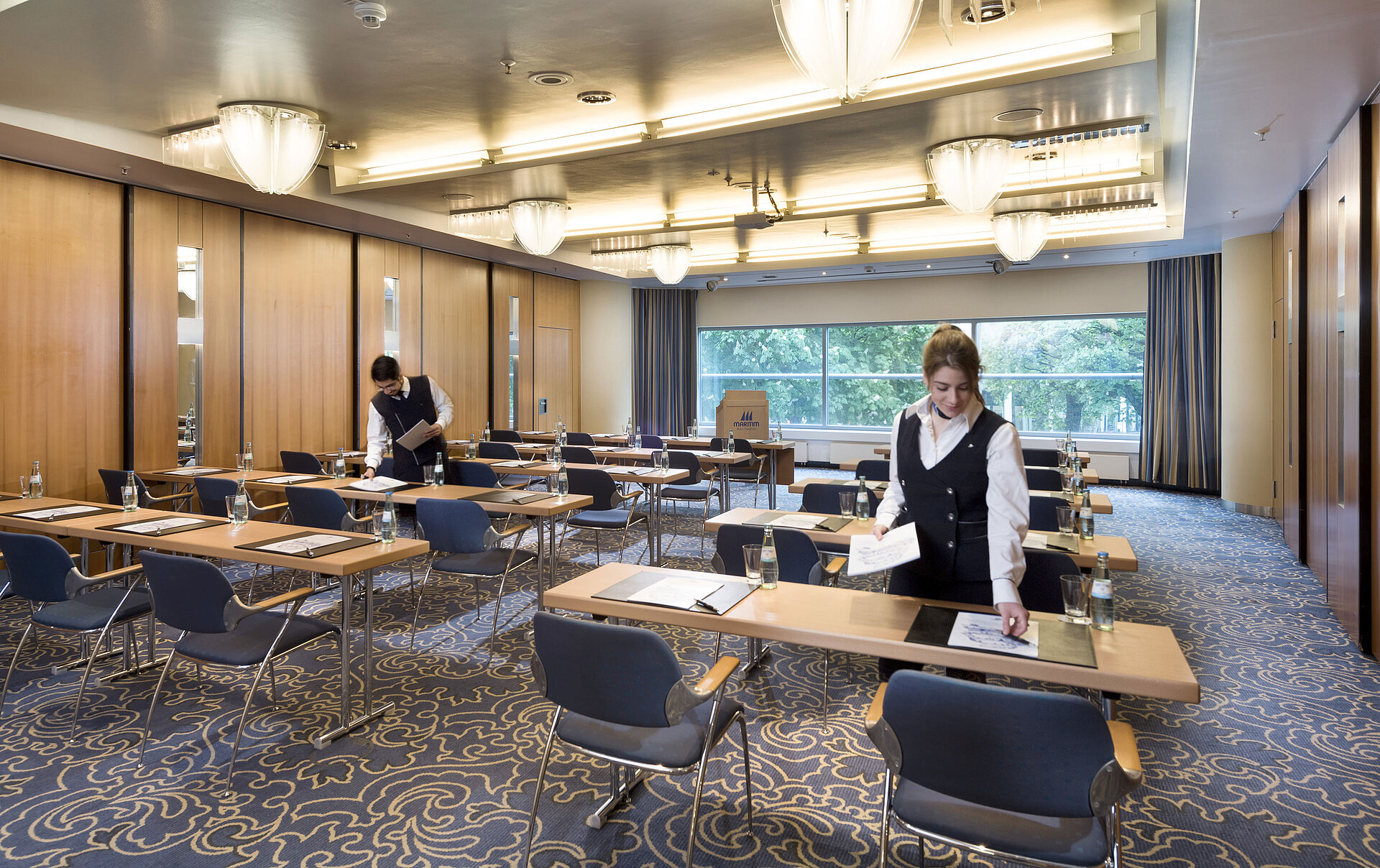 Saal Maritim II Parlament Mitarbeiterinnen bereiten einen Tagungsraum im Maritim Hotel Frankfurt mit Reihenbestuhlung und Blick ins Grüne vor.