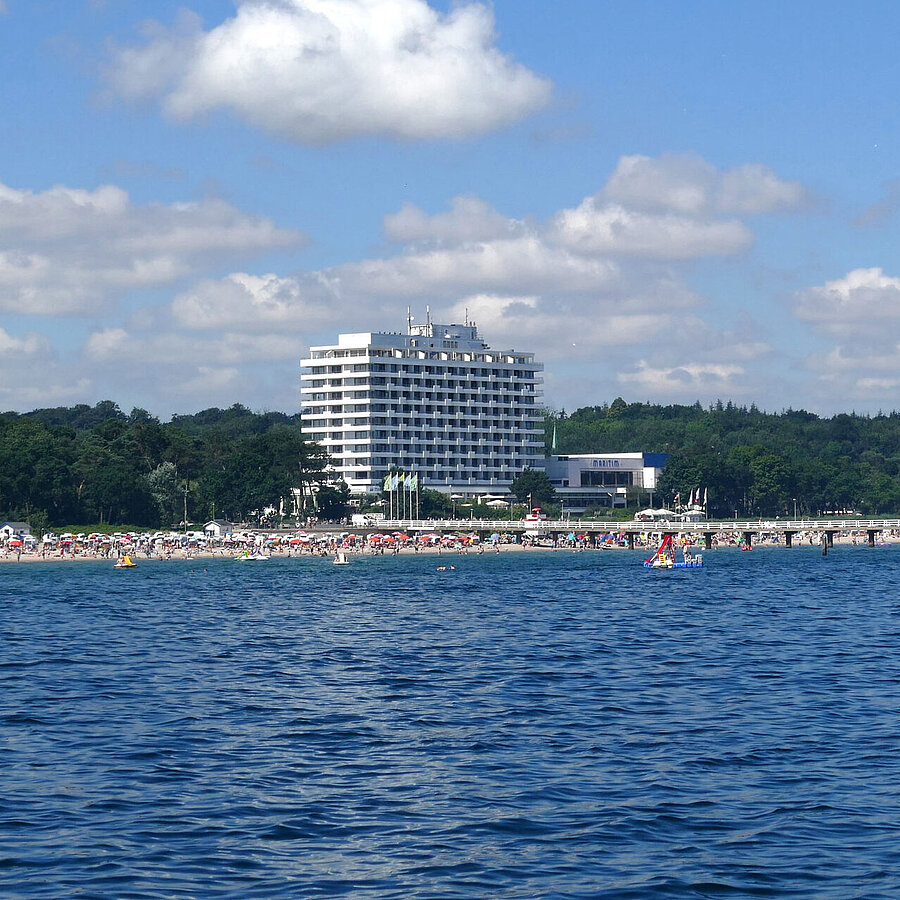 Maritim Seehotel Timmendorfer Strand, Seebrücke und bunte Flaggen vom Boot aus bei sonnigem Wetter.