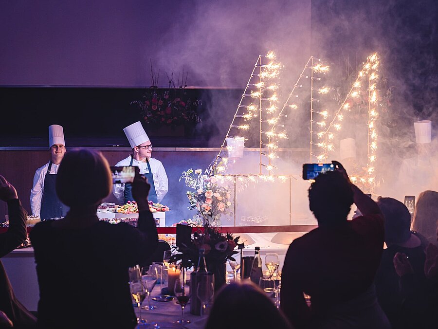Gäste verfolgen eine abendliche Bühnenshow mit Lichteffekten und Funken bei einer Veranstaltung