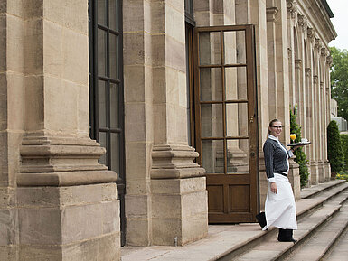 Freundliche Servicekraft serviert Frühstück mit frisch gepresstem Orangensaft auf der Terrasse des Maritim Hotel Fulda.