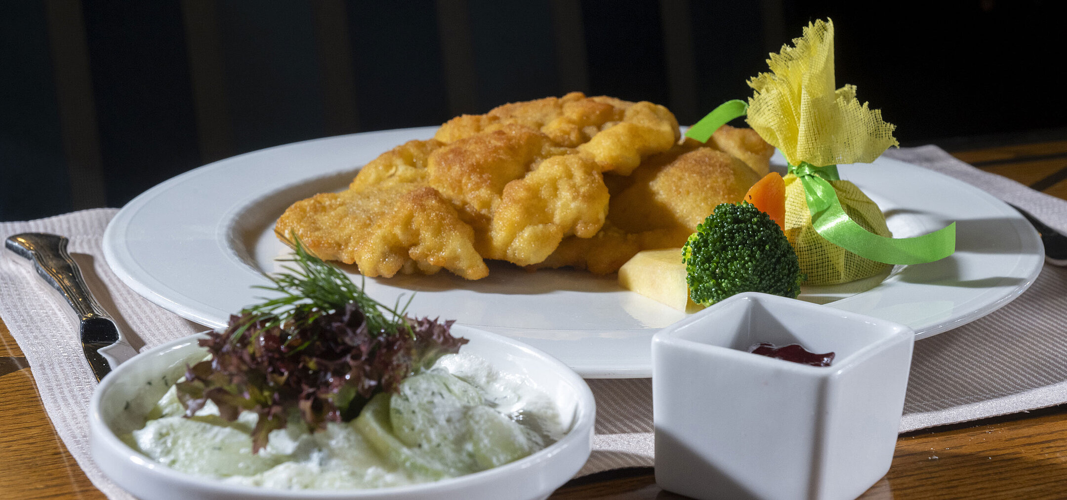 Knuspriges Wiener Schnitzel mit Gurkensalat, Preiselbeeren und Gemüse auf elegant angerichtetem Teller