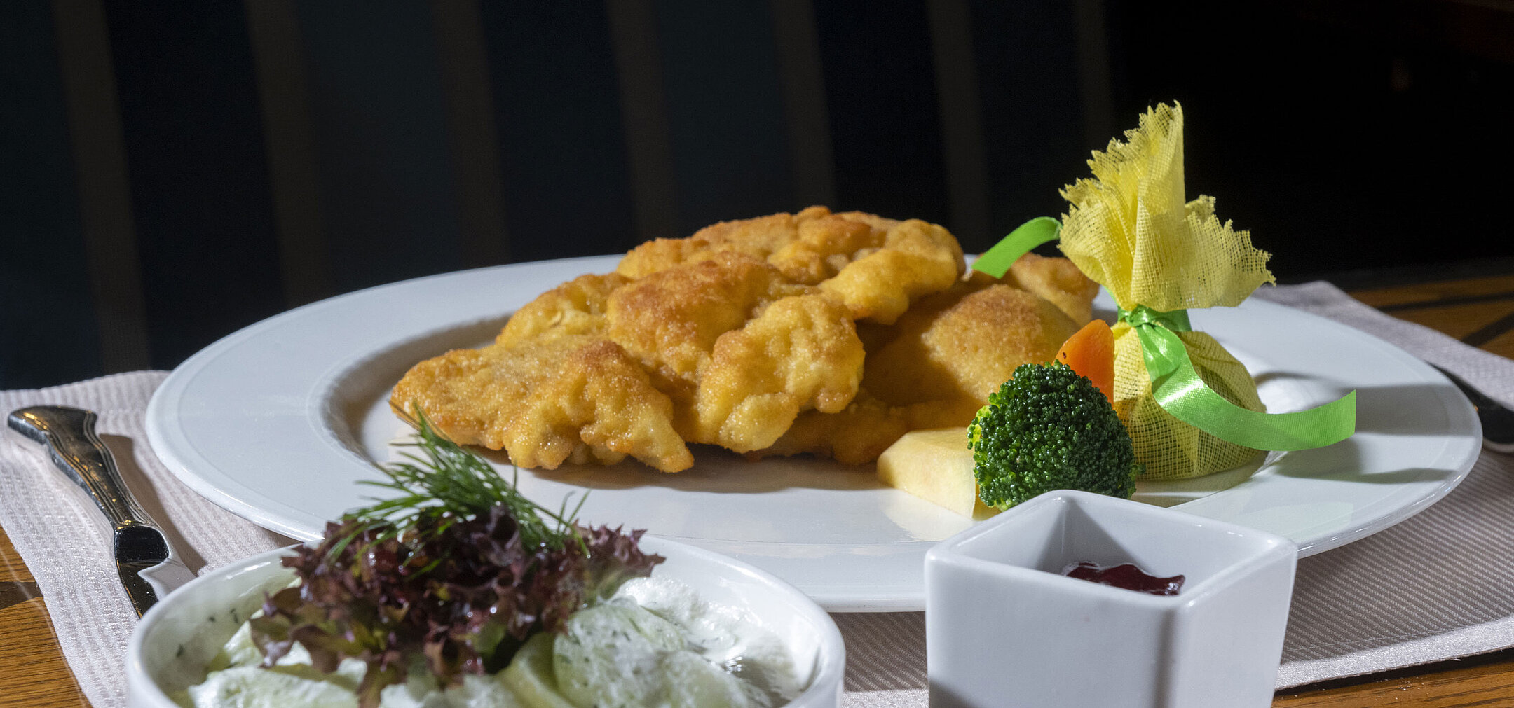 Knuspriges Wiener Schnitzel mit Gurkensalat, Preiselbeeren und Gemüse auf elegant angerichtetem Teller