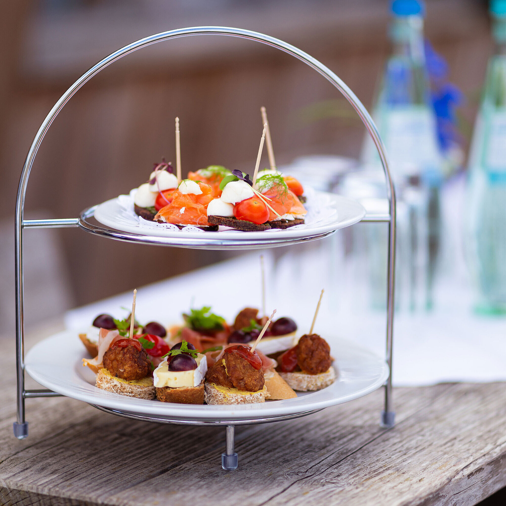  Elegant servierte Häppchen auf einer zweistöckigen Etagere, bereit für eine stilvolle Veranstaltung am Strand mit Getränken.