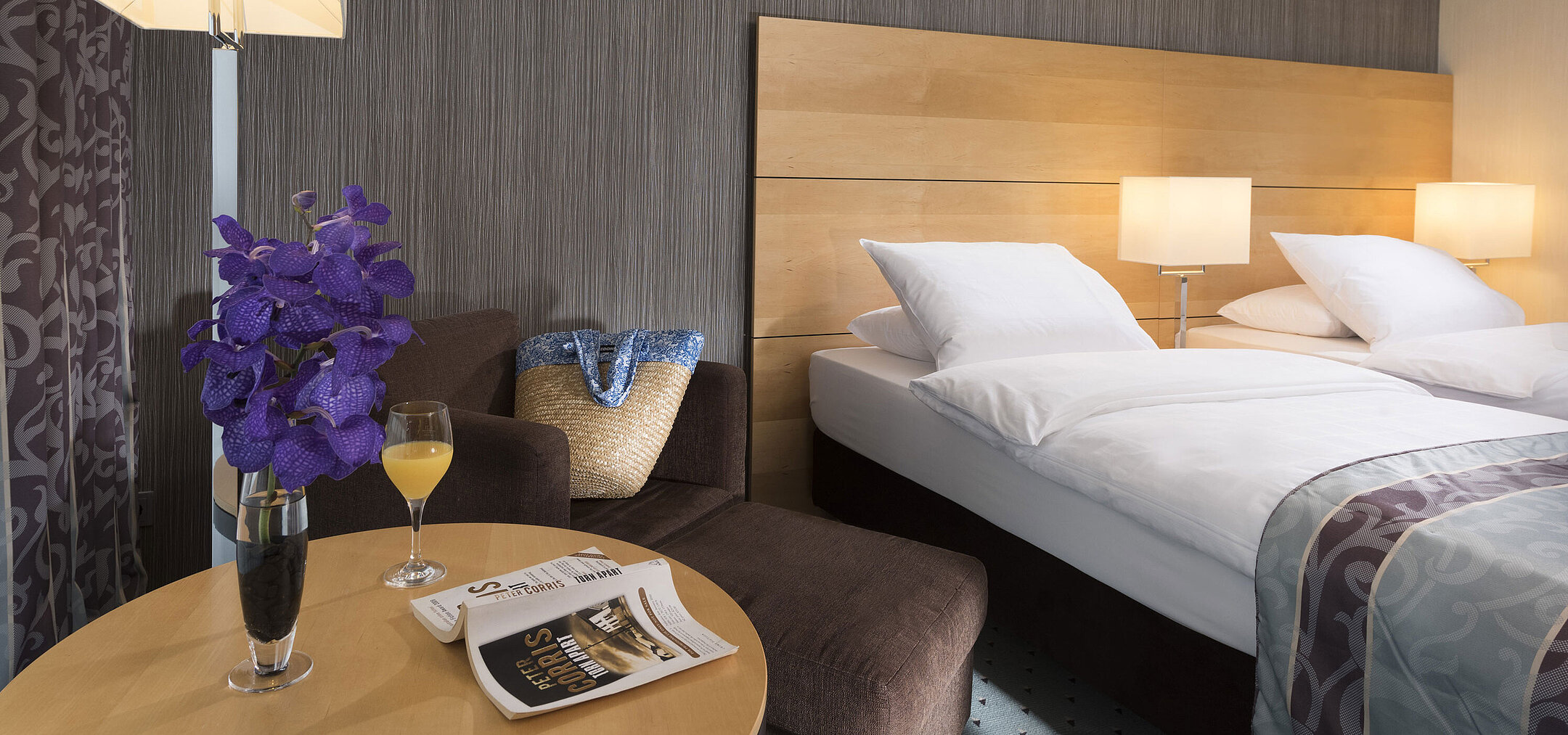 Classic Zimmer im Maritim Hotel Düsseldorf mit elegantem Doppelbett, gemütlicher Sitzecke, frischer Blume und Lesematerial.