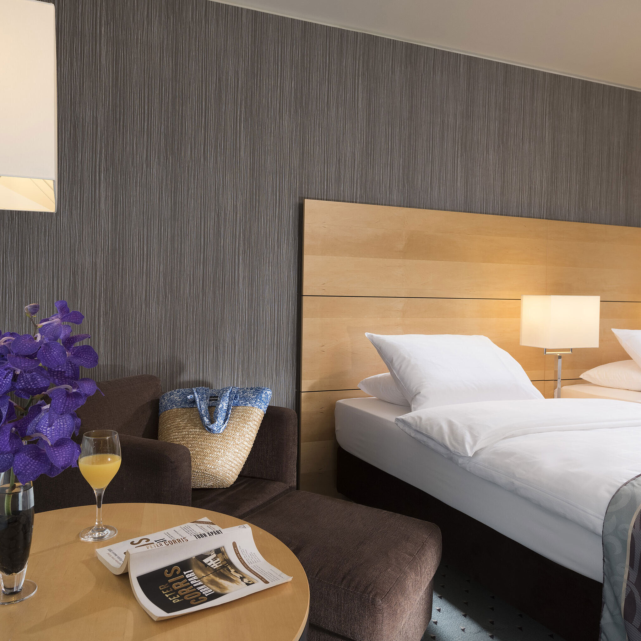 Classic Zimmer im Maritim Hotel Düsseldorf mit elegantem Doppelbett, gemütlicher Sitzecke, frischer Blume und Lesematerial.