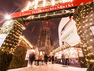 Ulmer Weihnachtsmarkt Eingang Ulmer Weihnachtsmarkt mit beleuchteten Ständen und Münster im Hintergrund