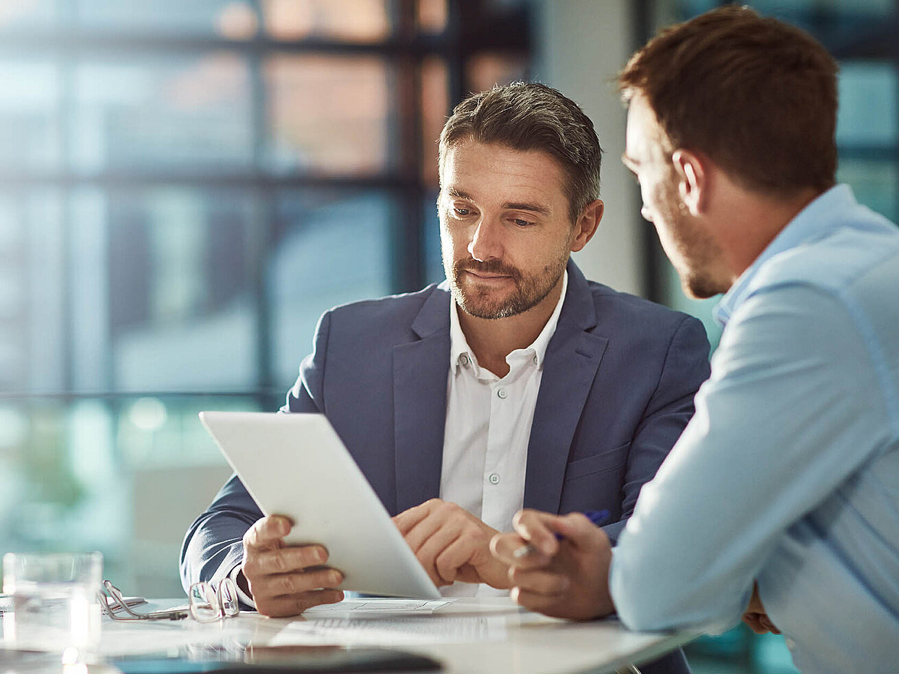 © Grady Rpeopleimages - Adobestock.com Zwei Geschäftsmänner im Büro besprechen Unterlagen auf einem Tablet.