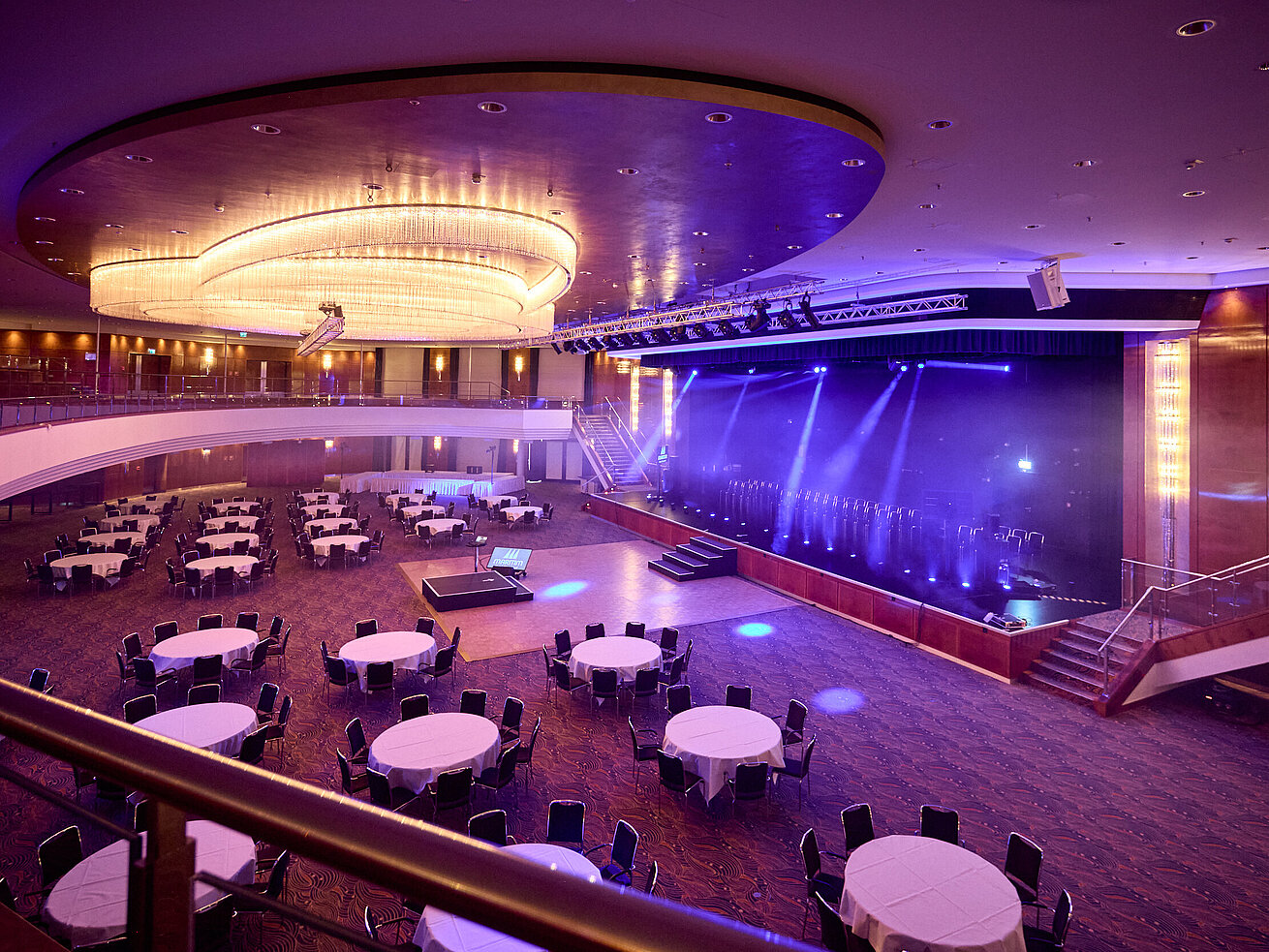 Großer Ballsaal mit Bühne, runden Tischen und moderner Lichttechnik für Gala oder Tagung.