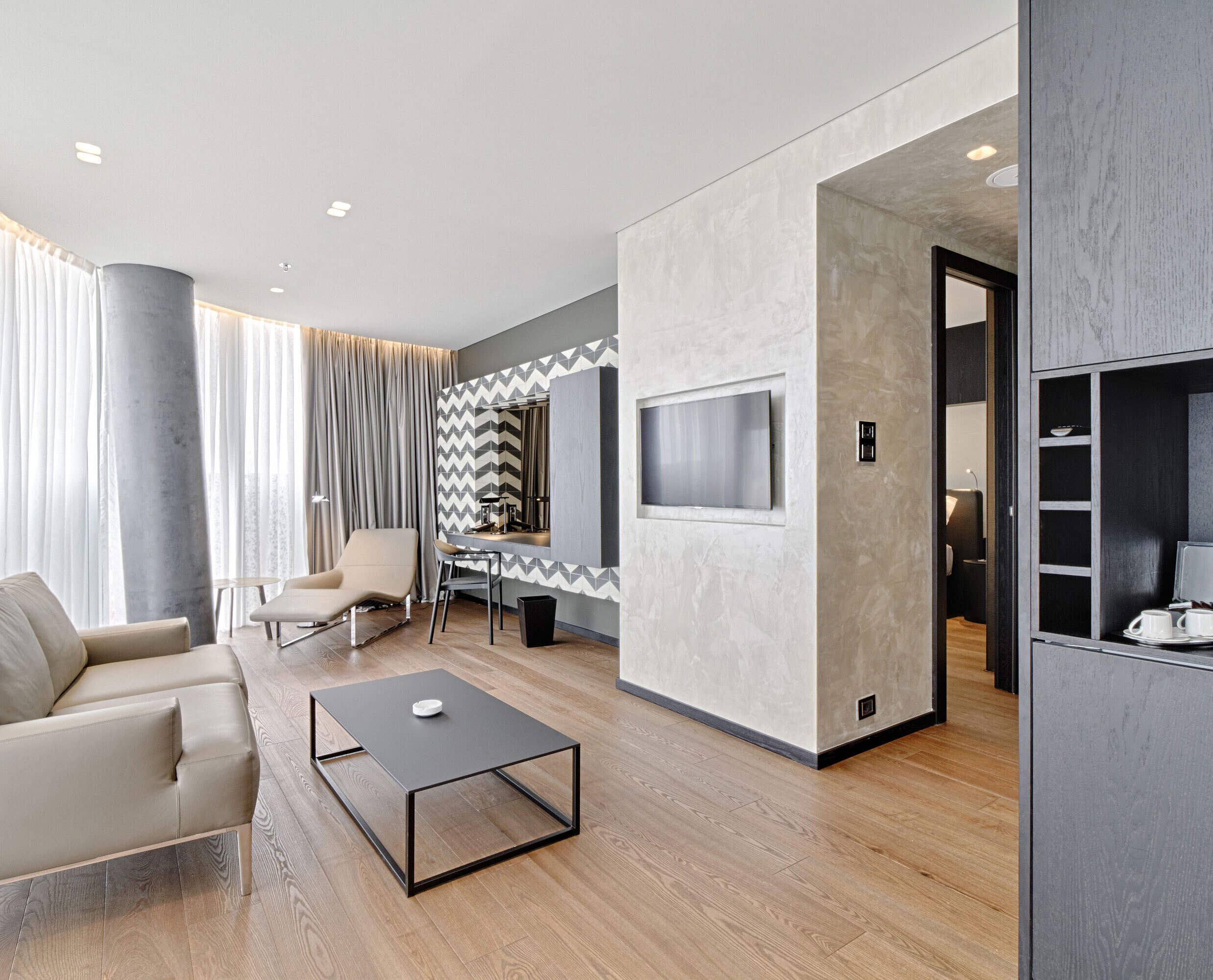 Lounge mit Sofa, TV, Designspiegel und Relaxliege im Maritim Hotel Plaza Tirana mit Tageslicht