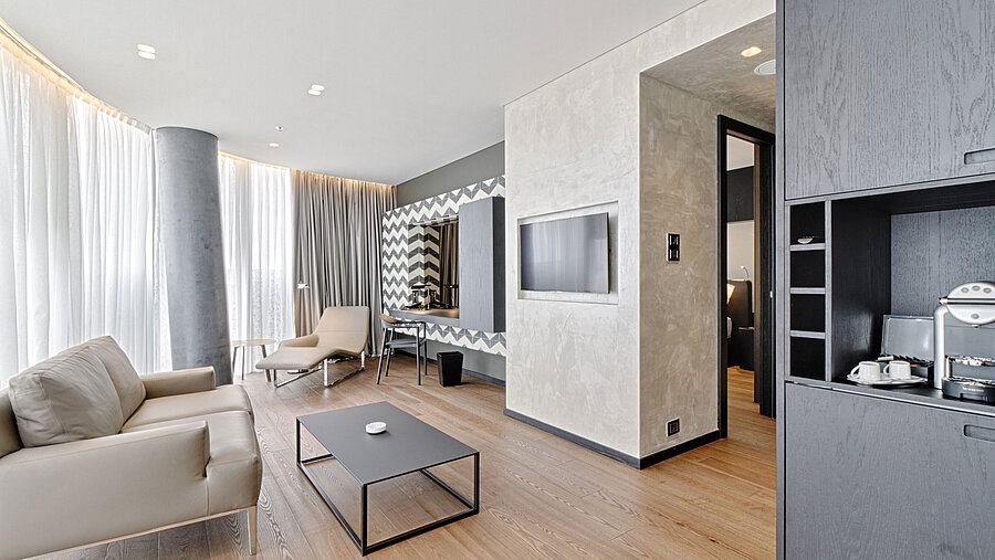 Lounge mit Sofa, TV, Designspiegel und Relaxliege im Maritim Hotel Plaza Tirana mit Tageslicht