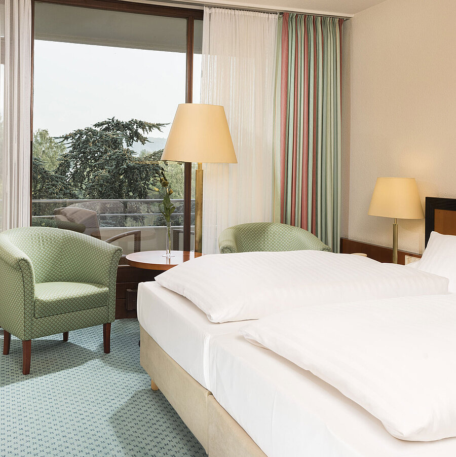 Helles Hotelzimmer im Maritim Hotel Bad Salzuflen mit Doppelbett, Sitzbereich und Zugang zum Balkon mit Ausblick