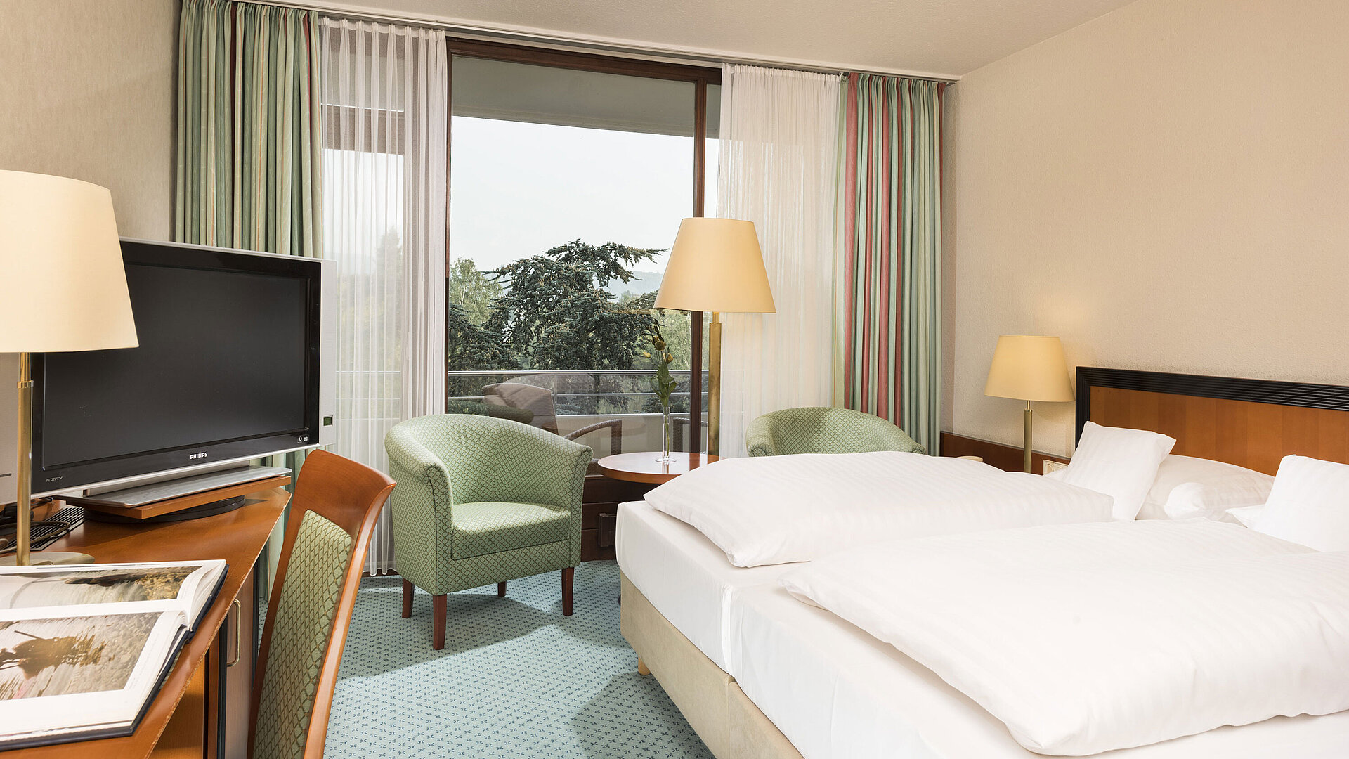 Helles Hotelzimmer im Maritim Hotel Bad Salzuflen mit Doppelbett, Sitzbereich und Zugang zum Balkon mit Ausblick