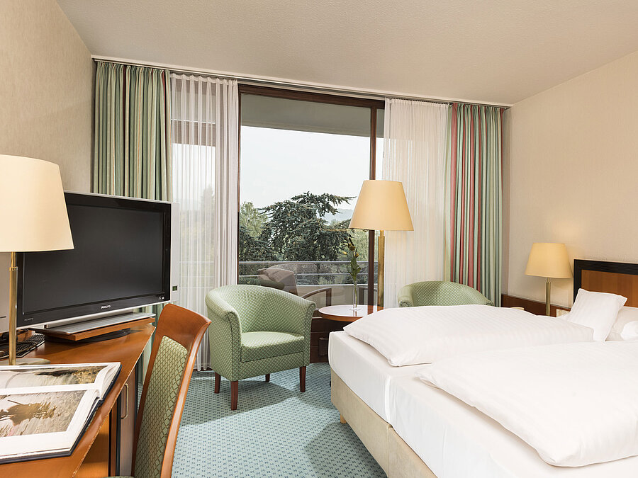 Helles Hotelzimmer im Maritim Hotel Bad Salzuflen mit Doppelbett, Sitzbereich und Zugang zum Balkon mit Ausblick