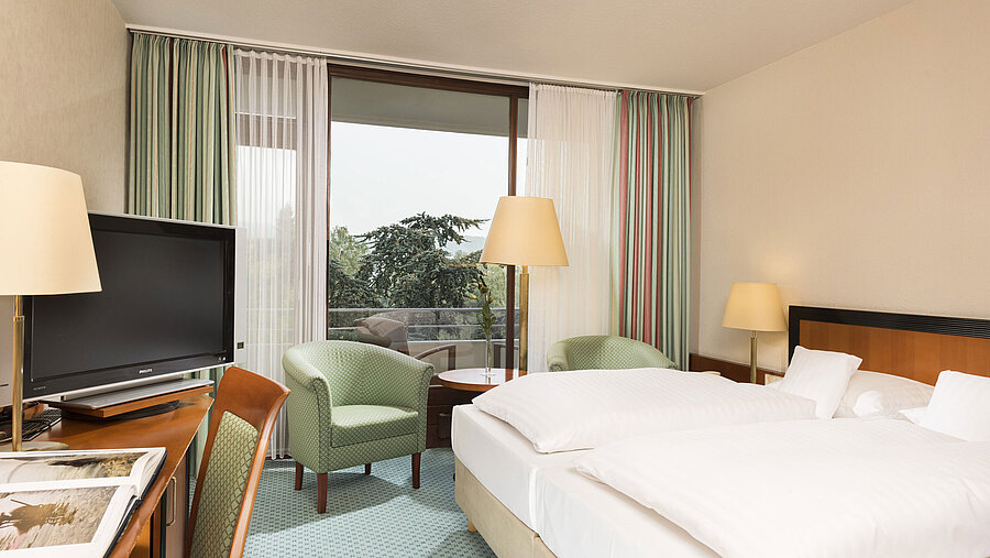 Helles Hotelzimmer im Maritim Hotel Bad Salzuflen mit Doppelbett, Sitzbereich und Zugang zum Balkon mit Ausblick