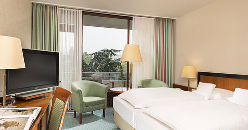 Helles Hotelzimmer im Maritim Hotel Bad Salzuflen mit Doppelbett, Sitzbereich und Zugang zum Balkon mit Ausblick