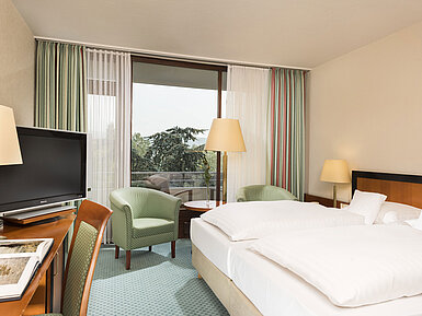 Helles Hotelzimmer im Maritim Hotel Bad Salzuflen mit Doppelbett, Sitzbereich und Zugang zum Balkon mit Ausblick