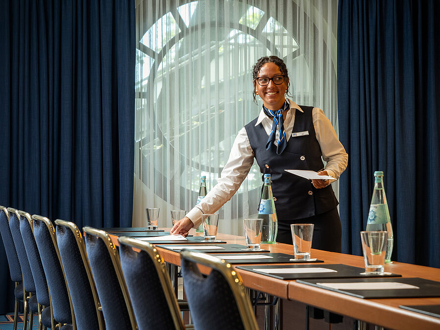 Tagungsservice Mitarbeiterin im Maritim Hotel Köln bereitet Konferenzraum mit Getränken und Unterlagen vor