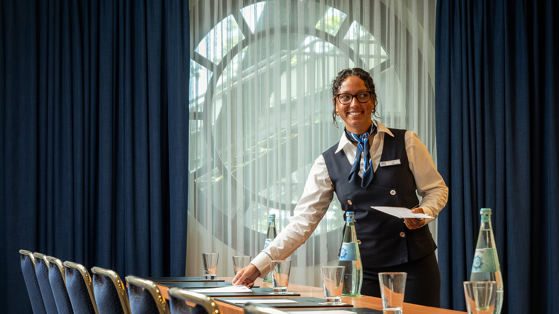 Mitarbeiterin im Maritim Hotel Köln bereitet Konferenzraum mit Getränken und Unterlagen vor