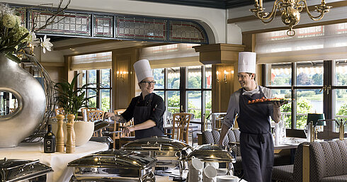 Zwei Köche am Buffet des Maritim Hotel Königswinter bereiten frisch angerichtete Speisen mit Blick auf den Rhein zu.