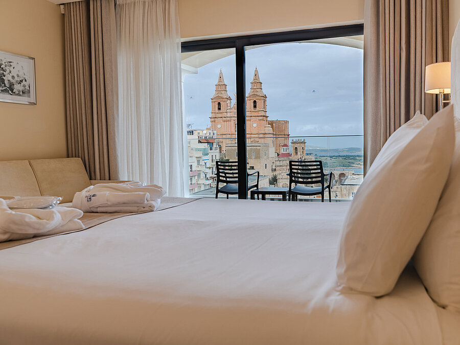 Hotelzimmer mit Doppelbett, Balkon und Blick auf historische Kirche und Stadt