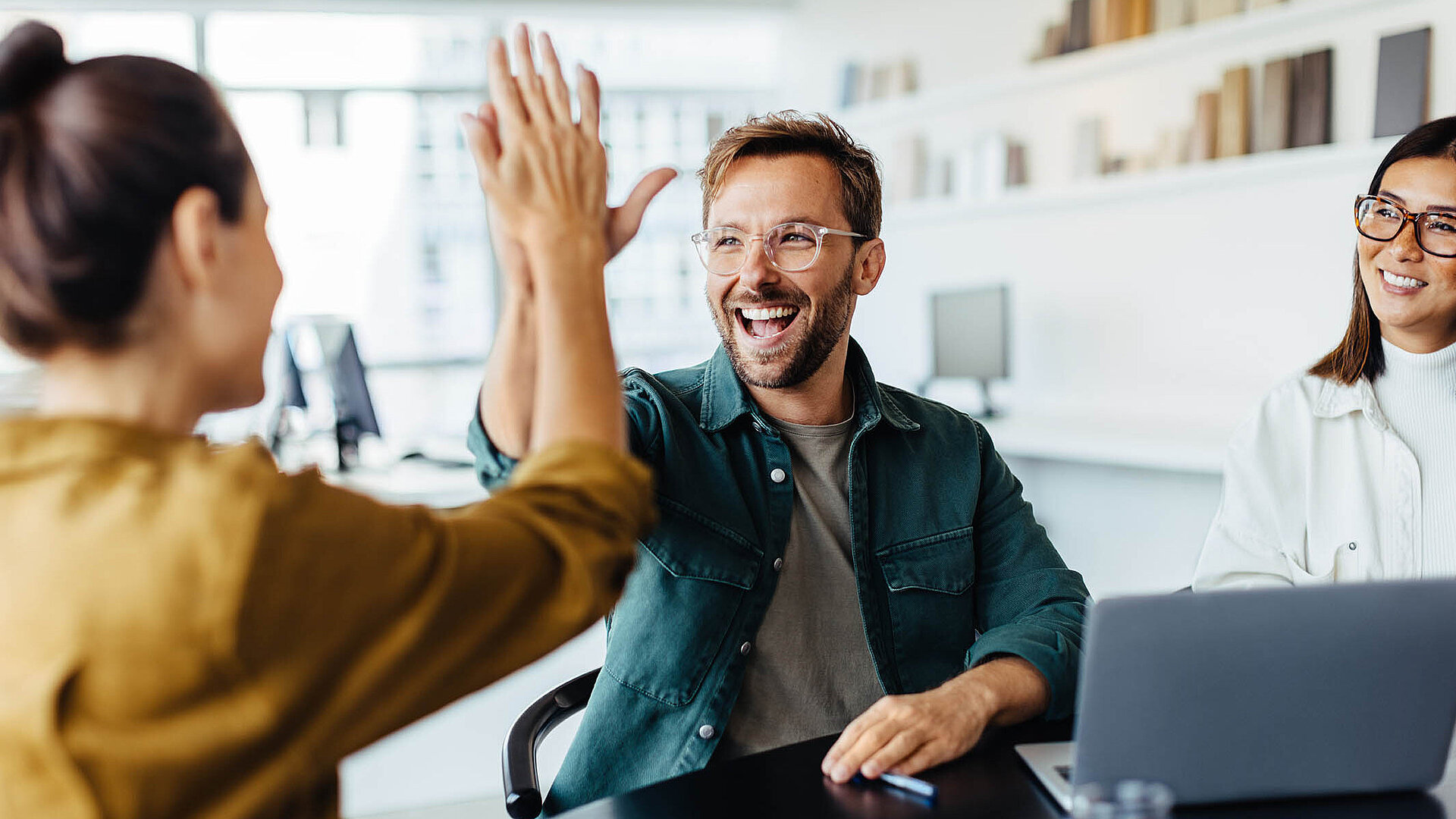 Zwei Kollegen im Büro geben sich lachend ein High Five als Zeichen erfolgreicher Teamarbeit.