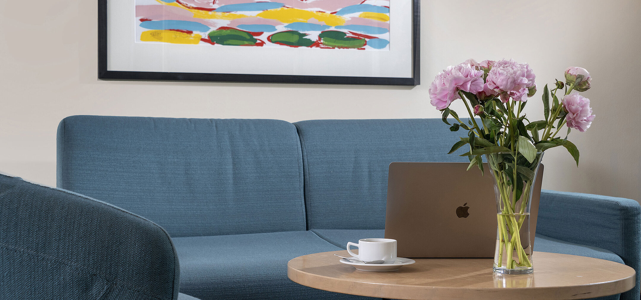 Moderner Wohnbereich mit Sofa, Couchtisch, Blumenstrauß und Laptop im Maritim proArte Hotel Berlin