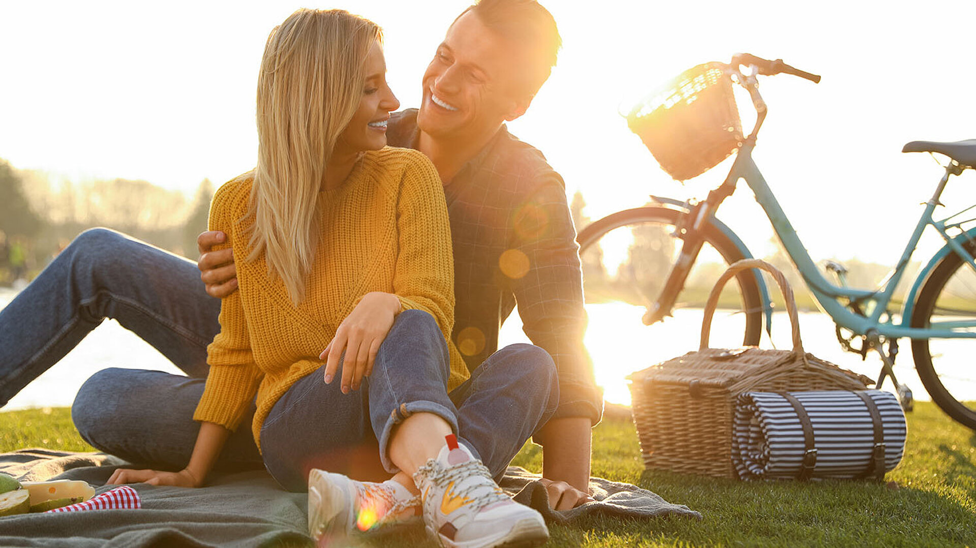 © New Africa - AdobeStock.com Paar genießt ein Picknick auf einer Wiese neben Fahrrädern bei sonnigem Wetter