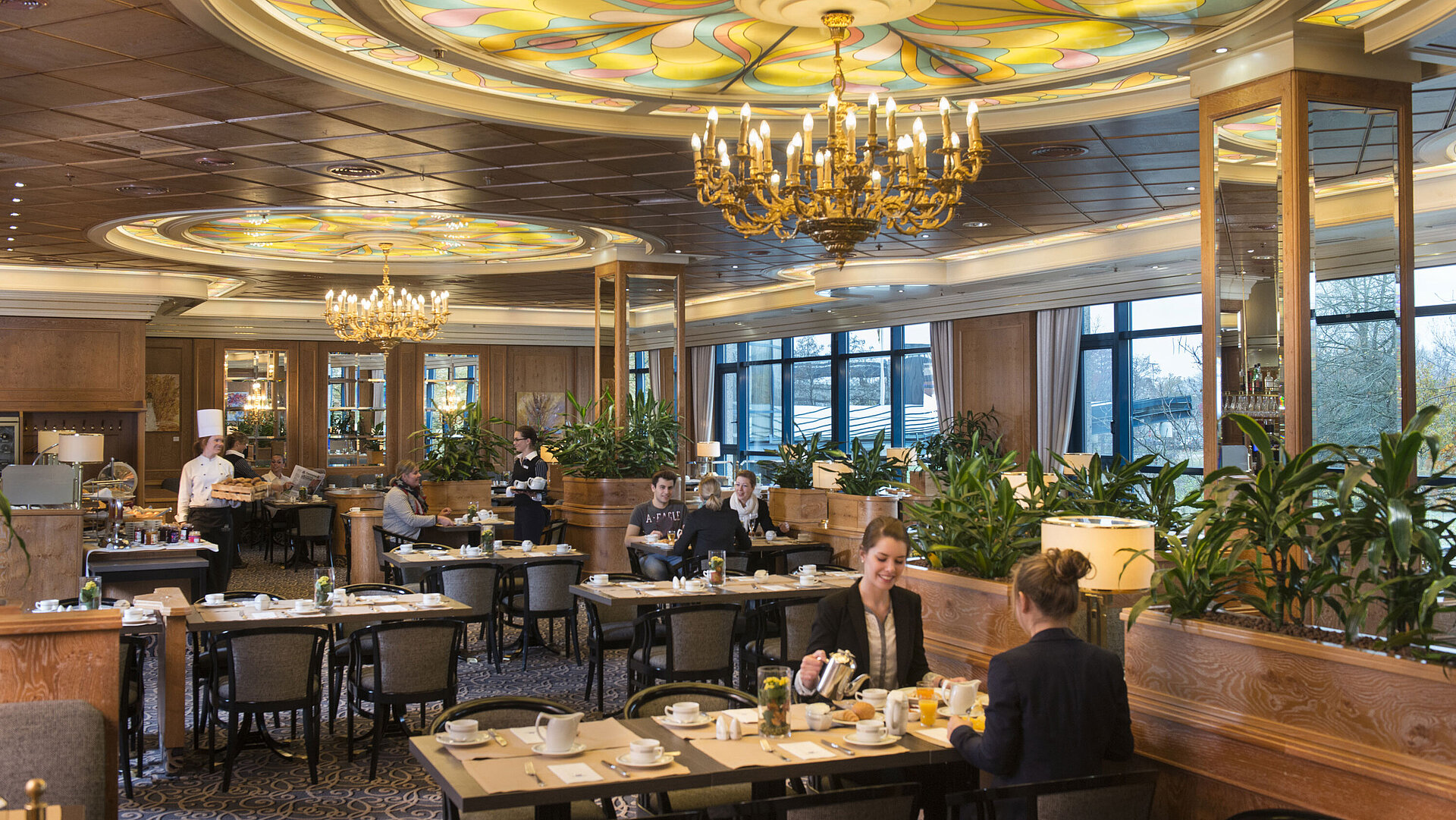 Gäste genießen Frühstück im stilvollen Restaurant mit Kronleuchtern und großen Fenstern im Maritim Hotel Hannover.