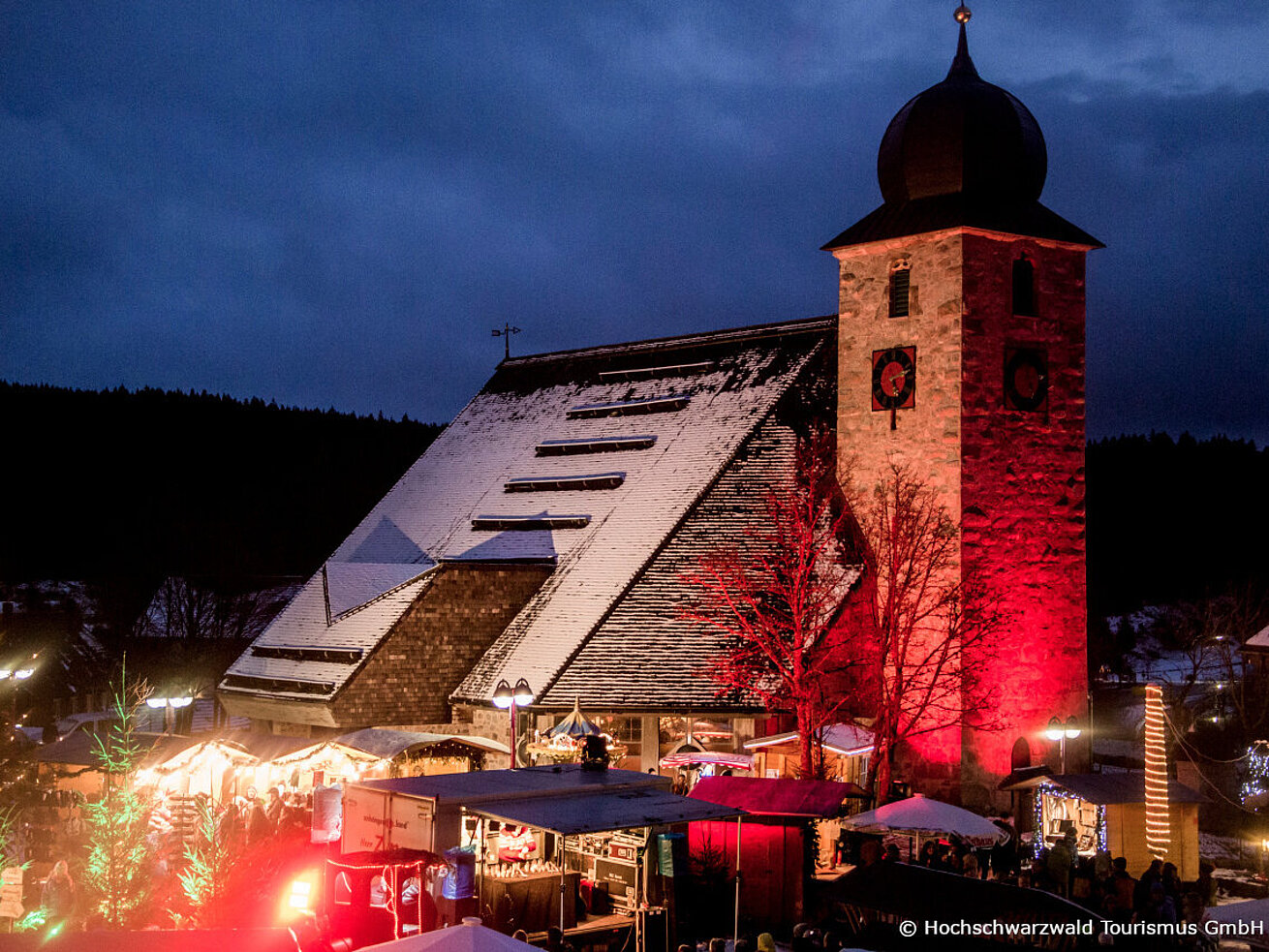 Wintermarkt am Schluchsee mit beleuchteter Kirche, Ständen und festlicher Abendstimmung.