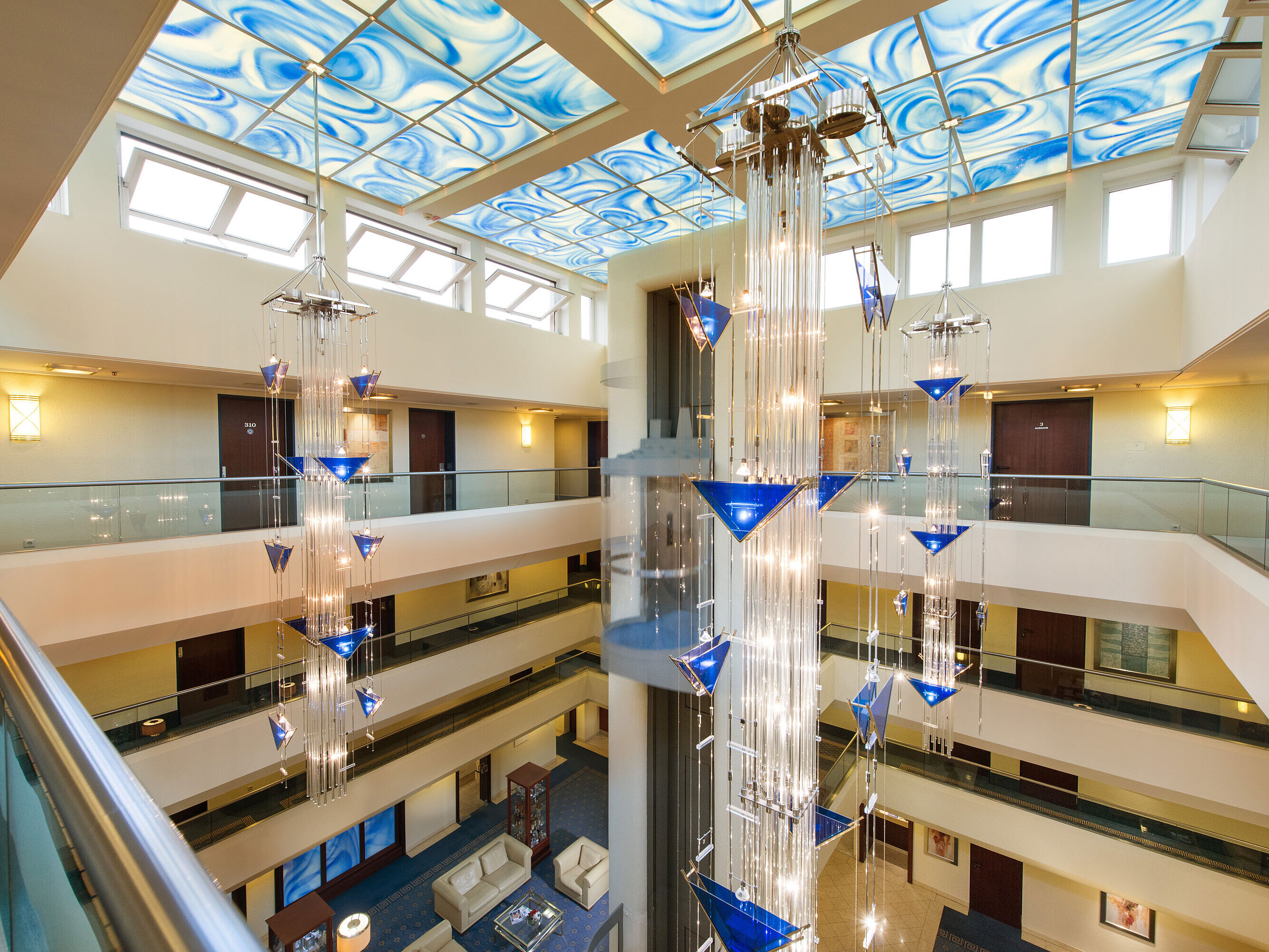 Modernes Atrium im Maritim Hotel Fulda mit gläsernem Aufzug, blauem Deckendesign und kunstvollem Kronleuchter.