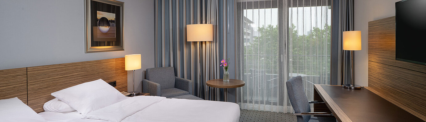 Gesamtansicht des Comfort Zimmers im Maritim Hotel Darmstadt mit Bett, Schreibtisch und Zugang zum Balkon