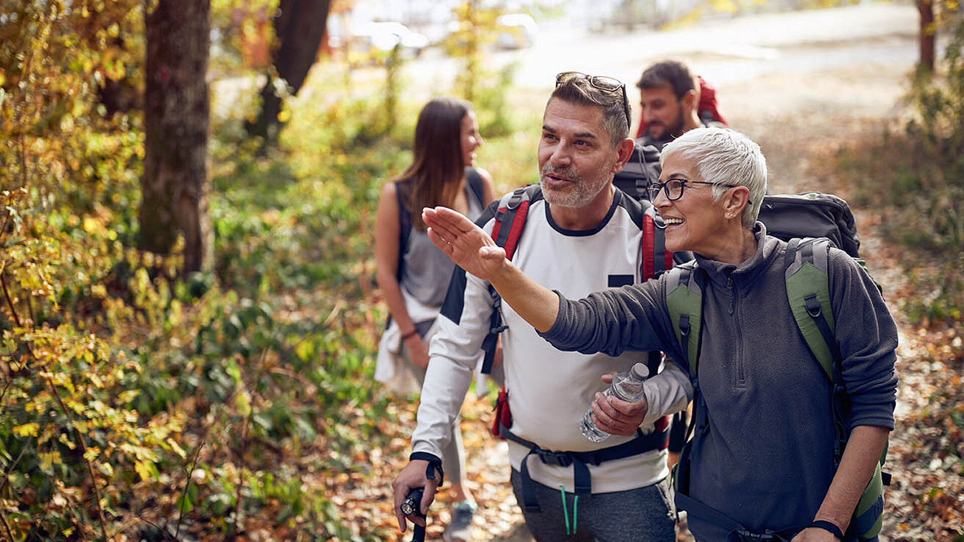Fröhliche Wandergruppe im Wald, Frau zeigt Richtung während der Herbstwanderung.  Titel: Gemeinsame Wanderung