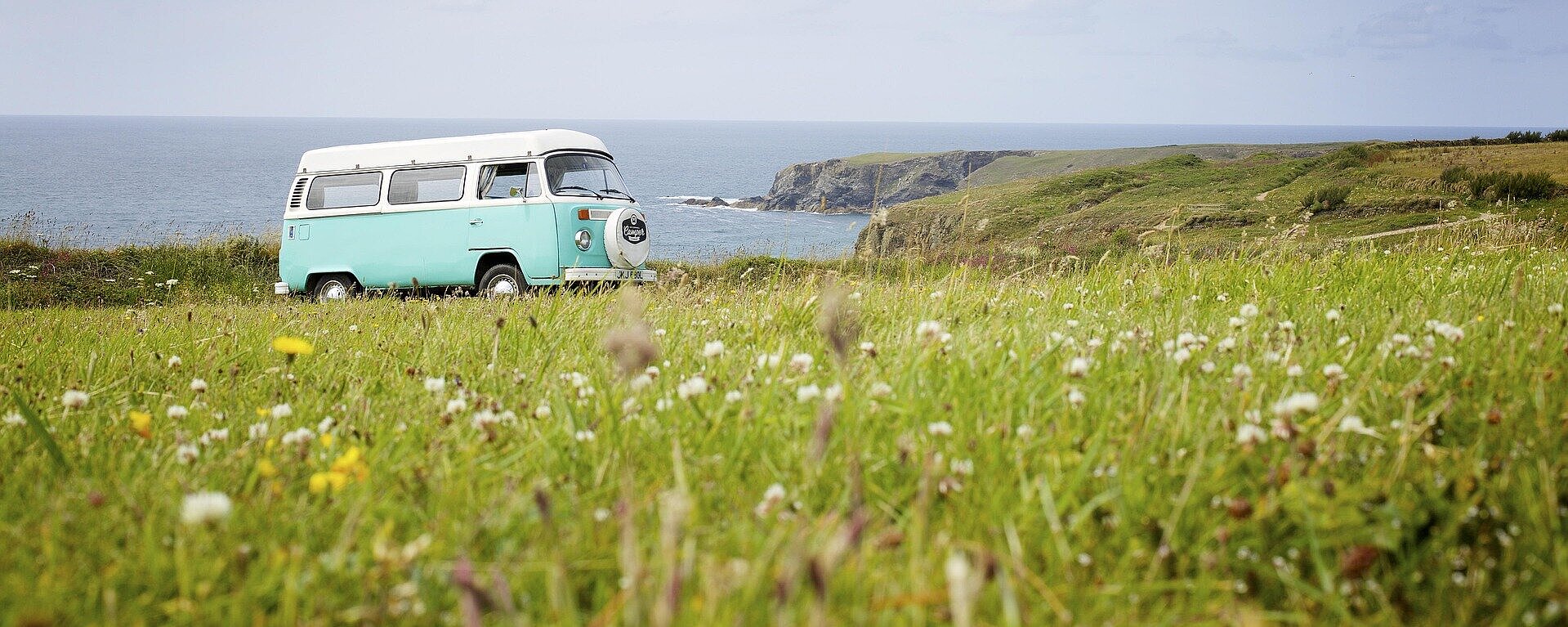 Retro-VW-Bus auf einer Wiese mit Blick auf das Meer und die Küste – perfekter Start ins nächste Abenteuer