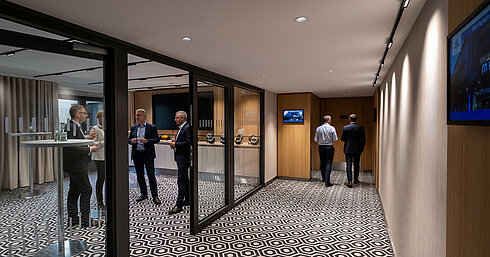 Kaffeepausen-Bereich mit Stehtischen, Kaffeemaschine und Gästen im Gespräch während einer Tagung.